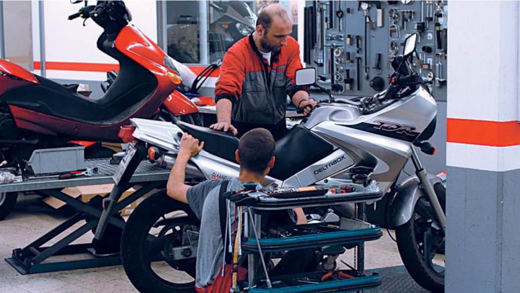 Photo d'un atelier où deux personnes travaillent sur une moto.